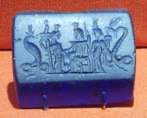 Petite plaque de verre bleu en relief : cinq divinités debout côte à côte, dont deux figures à corps de serpent aux extrémités.