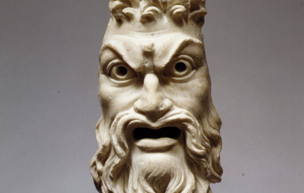 Masque en marbre d'un visage barbu aux traits rudes, la chevelure hérissée d'où émergent deux cornes brisées.