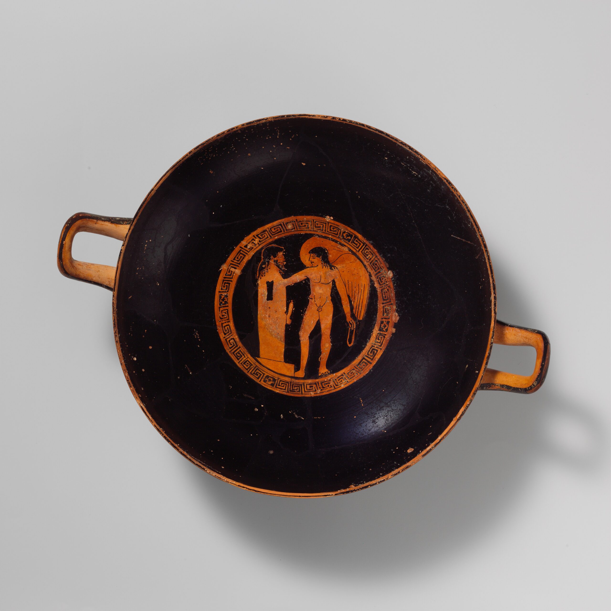 Médaillon intérieur d'une coupe grecque à figures rouges : une figure ailée devant un pilier surmonté d'une tête barbue.