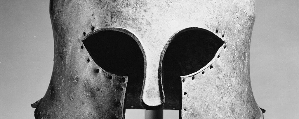 Casque de bronze grec vu de profil, avec des découpes pour les yeux, un nasal étroit et une ouverture pour la bouche.