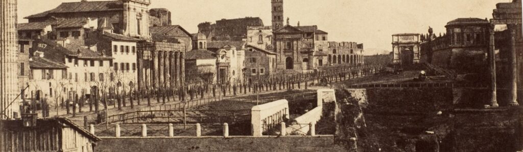 Photographie ancienne du Forum romain : au premier plan une balustrade et un terrain en chantier, au centre une allée d'arbres bordée d'églises et de maisons, au fond l'arc de Titus.