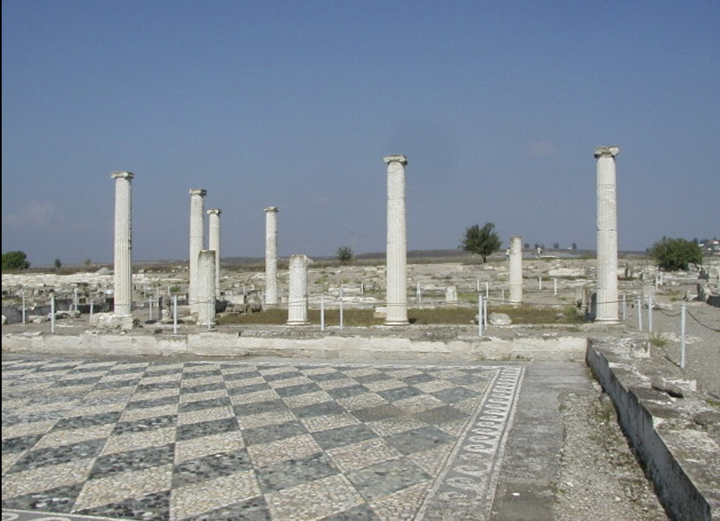 Sol d'une cour antique pavé de galets formant un motif géométrique, bordé de colonnes.