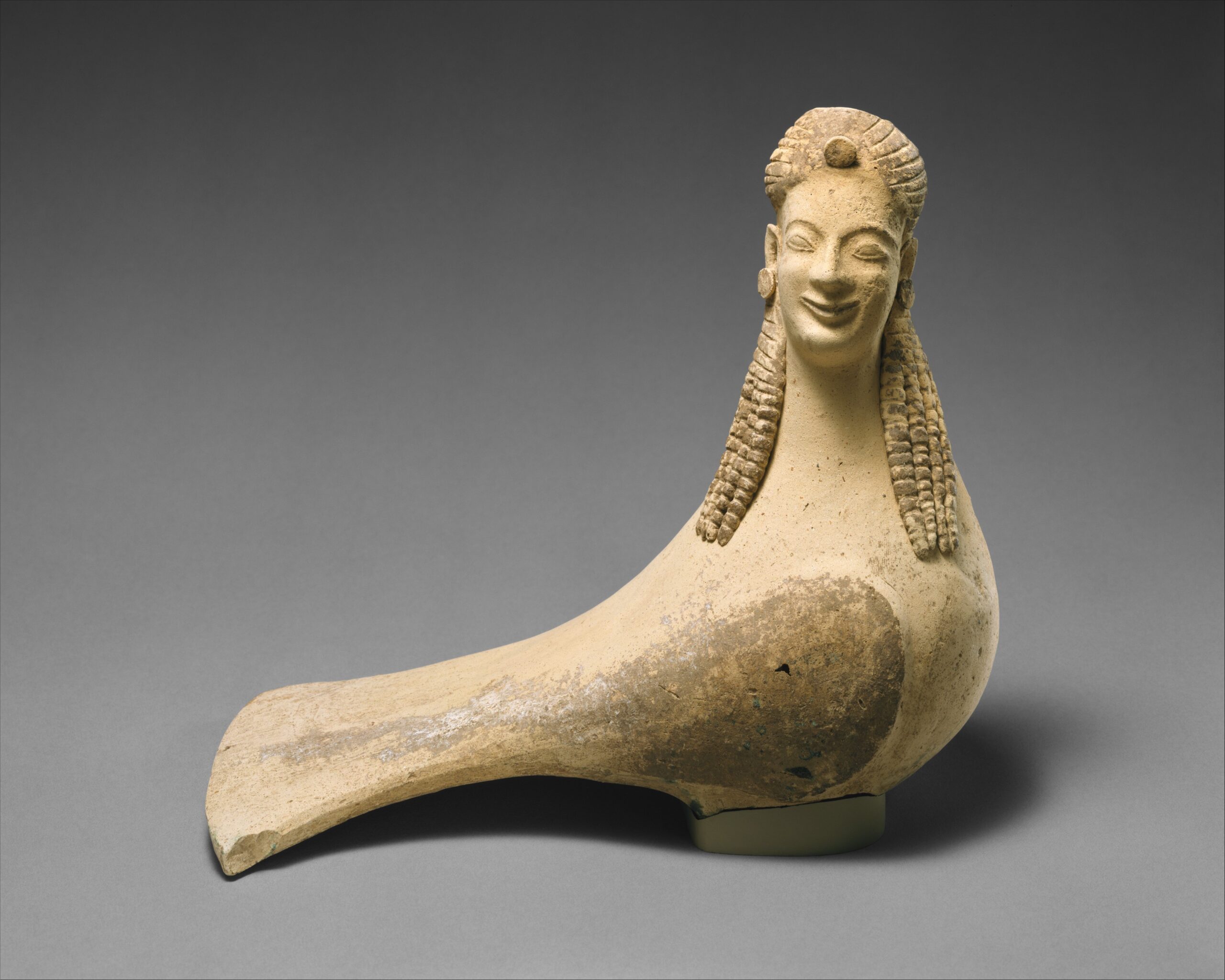 : Statuette en terre cuite représentant une créature au visage humain encadré de longs cheveux, posée sur un corps d'oiseau.