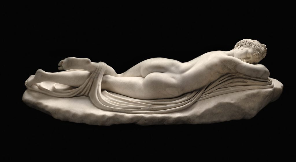 Statue en marbre d'une figure allongée sur le ventre sur un rocher drapé d'étoffe, la tête reposant sur les bras repliés.