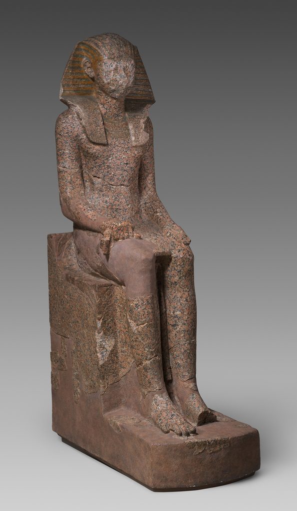 Grande statue assise en granite, coiffée du némès, le visage entièrement martelé, les mains posées sur les genoux.