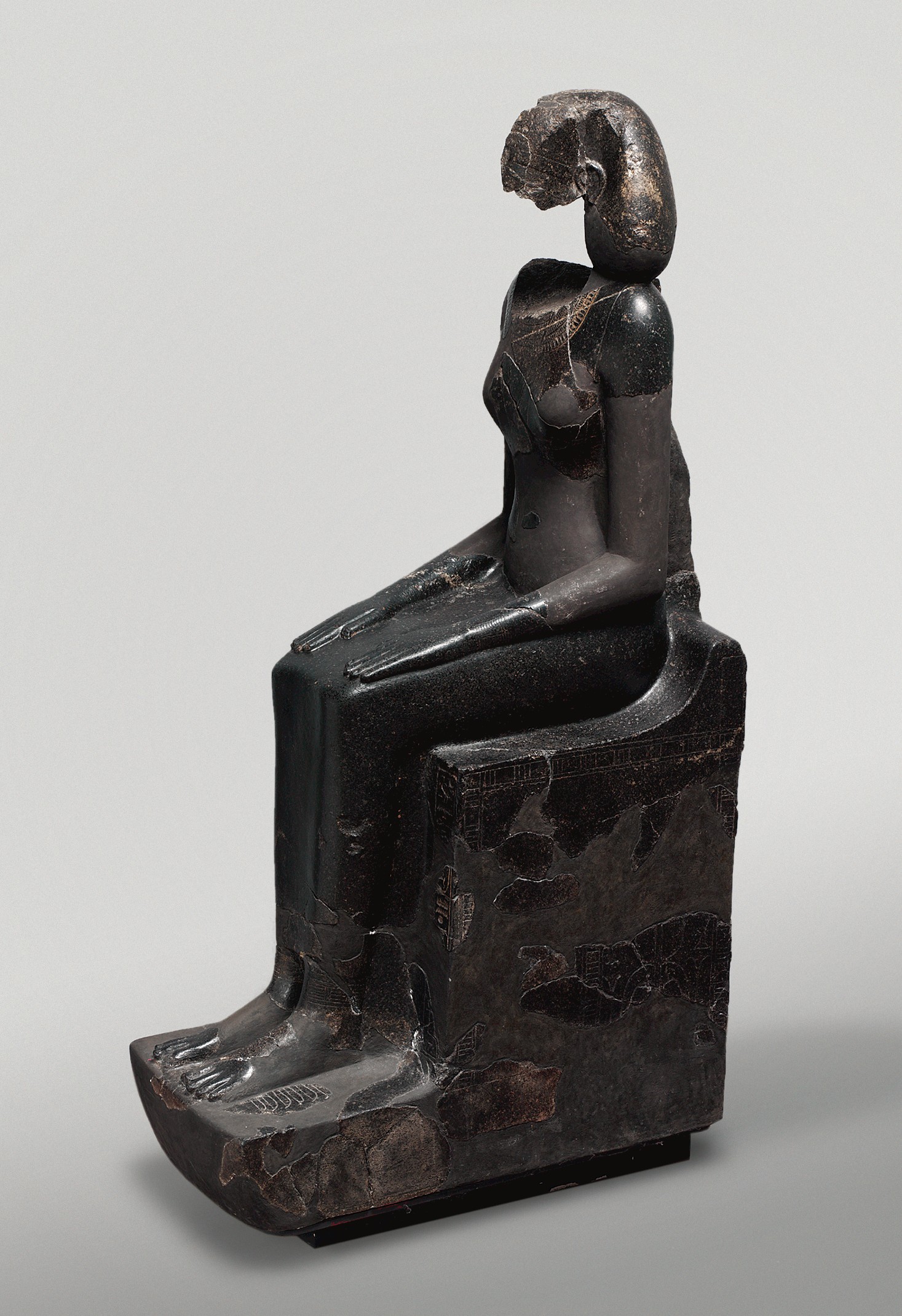 Statue en diorite d'une figure assise sur un trône, la tête coiffée d'un voile souple, les mains posées à plat sur les genoux.