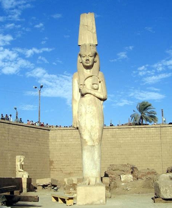 Statue en calcaire d'une femme coiffée d'une haute couronne à plumes, le visage souriant.