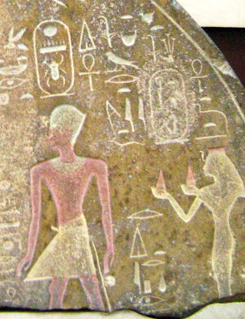 Stèle gravée montrant une femme debout derrière un homme, tenant des offrandes dans les mains.