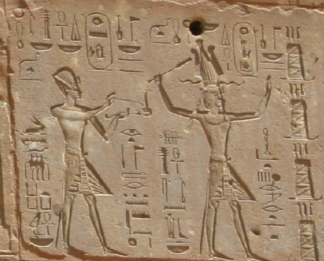 Bas-relief gravé montrant deux personnages debout se faisant face, les bras levés, au milieu de colonnes de hiéroglyphes.